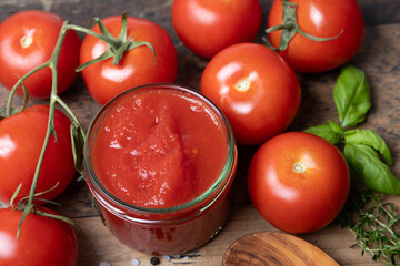 homemade tomato sauce in glass jar, with ingredients basil, thyme, salt, pepper, stands on a wooden table with shabby look,