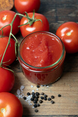 Traditional italian homemade tomato sauce in glass jar, with  salt, pepper, stands on a old wooden table, portrait format