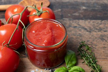 homemade tomato sauce in glass, with ingredients basil, thyme, salt, pepper, stands on a wooden table with shabby look, space for text