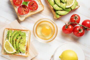 Variation of healthy breakfast toasts with avocado and cherry tomatoes on white wooden background....