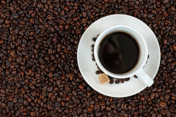 Black coffee in a white cup on a background of coffee beans top view. 