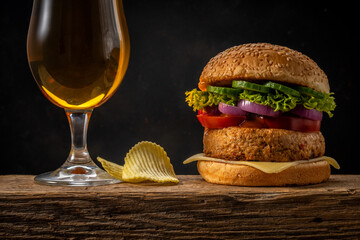 View of fresh tasty burger with glass of beer on wooden rustic table. Food background.