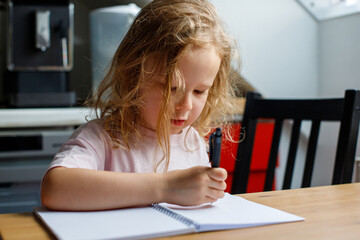 Close-up of a girl of 4s drawing in a notebook in the kitchen of the house. upbringing of children. children's leisure time. home upbringing of a child