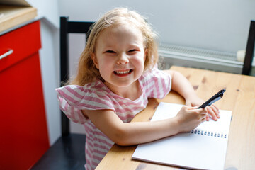 blonde little girl drawing something in in the kitchen