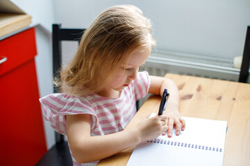Close up photo of a blonde little girl drawing something in her notebook
