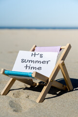 IT'S SUMMERTIME text on paper greeting card on background of beach chair lounge summer vacation...