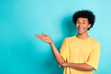 Photo of positive guy with afro hairdo dressed yellow t-shirt palm indicating at offer empty space...