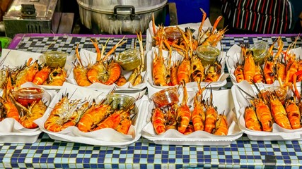 Vibrant display of grilled prawns arranged on take away plates, served with dipping sauces at street food market. Fresh, colorful seafood showcases appeal of outdoor dining and local cuisine