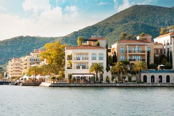 View from the sea to sunny beach of Mediterranean seaside town with palm trees, red rooftops...