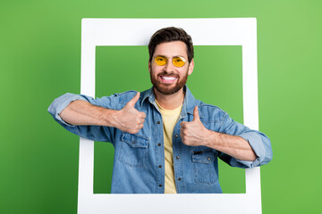 Photo of good mood confident guy dressed jeans shirt holding photo frame showing two thumbs up...