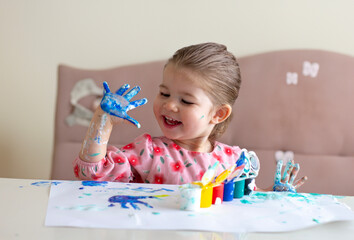 A blonde girl finger-painting. Her hands are painted blue. It's a fun moment.