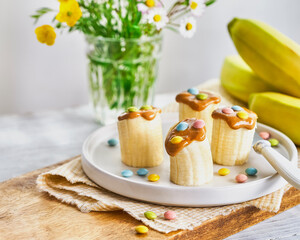 Banana healthy snacks with peanut butter, colorful sprinkles on a light wooden table. Close Up. Breakfat or brunch for kids. Selective focus.