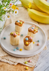Banana healthy snacks with peanut butter, colorful sprinkles, and a knife on a light wooden table. Ample space for text. Breakfat or brunch for kids.