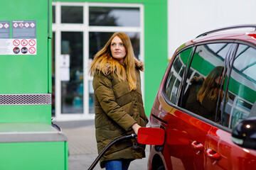 Young woman at self-service gas station, hold fuel nozzle and refuel the car with petrol, diesel, gas.