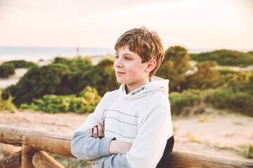 Happy cheerful teenager standing on beach at sunset. happy preteen boy smiling at the camera. Kid on family vacation at the sea.