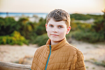 Happy cheerful teenager standing on beach at sunset. happy preteen handsome boy smiling at the camera. Kid on family vacation at the sea.