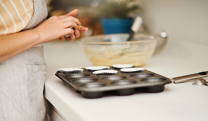 Baker hands, baking tray and cupcakes prepare in kitchen in house for relax or therapeutic hobby. Dessert, cooking and professional person with homemade for small business or home recipe with paper.