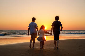 Three kids silhouettes running and jumping on beach at sunset. happy family, two school boys and...