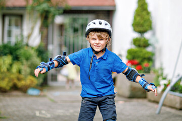 Portrait of little school kid boy in safety protection clothes scating with rollers. Active sporty child doing sports on summer day. Outdoor activity for kids.