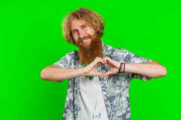 Man in love. Smiling attractive bearded man makes heart gesture demonstrates love sign expresses good positive feelings and sympathy. Handsome redhead young guy isolated on chroma key wall background