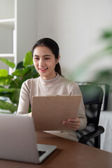Business woman working in office checking documents. Woman accounting executive using laptop reading paper file financial report, tax invoice