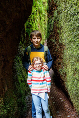 Teenager boy with backpack and little preschool girl hiking through a cave. Happy children, siblings, having fun with activity.
