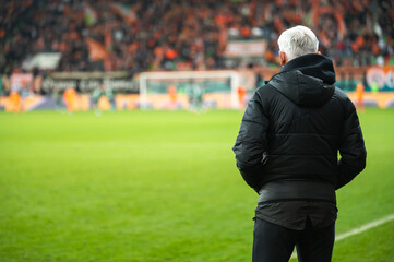 Head coach's back and soccer match at the stadium in the background.