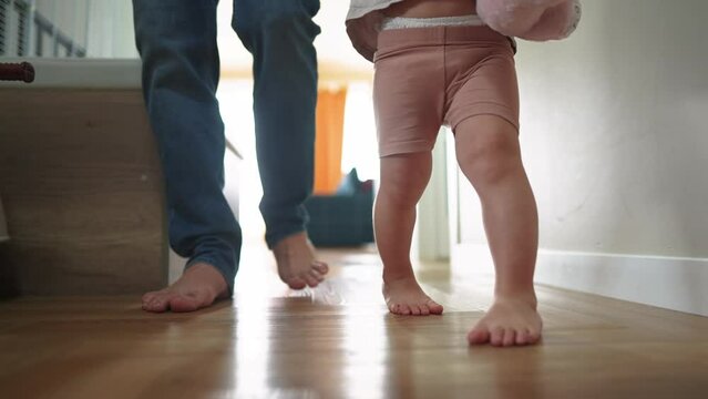 baby first steps with dad. happy family a kid dream concept. dad and baby daughter walk along the corridor of the house indoors. dad and daughter care, hold hands lifestyle, walk, take first steps