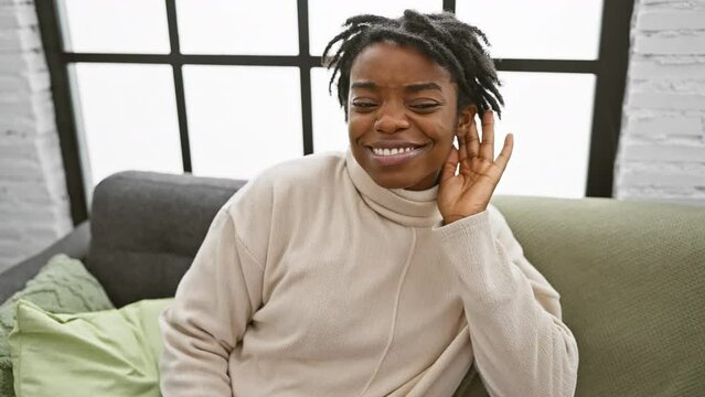 Young woman with dreadlocks, chillin' on the sofa at home, all ears to the hot gossip, cupping her hand to hear better. deafness ain&rsquo;t gonna rain on her parade!