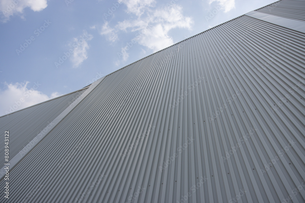 Poster a large factory building with a grey roof and a blue sky in the background