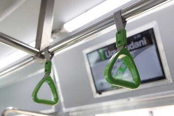 A green and silver hand rail in public train. The rail is attached to a metal pole.