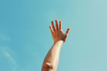 Single hand reaching upwards against a clear blue sky
