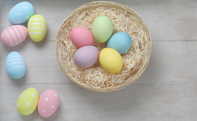 Easter nest with eggs in pastel colors like yellow, green, purple, pink and yellow in and outside the nest, which is standing on a wooden table.