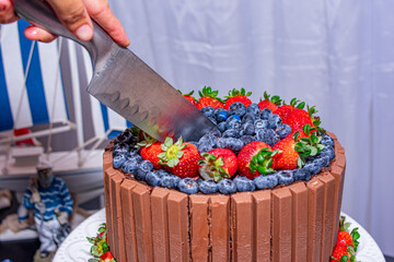 bolo de aniversário de chocolate, morango e mirtilos com uma pá cortando o bolo