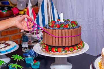 bolo de aniversário de chocolate, morango e mirtilo com uma mão soltando o laço.