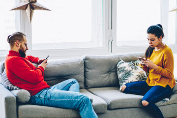 Young family sitting on sofa in living room using smartphone ignore real conversation  blogging and...