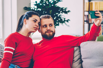 Romantic hipster couple posing for selfie on smartphone camera,young male holding mobile phone for taking picture with his girlfriend spending free time together sitting on couch at home interior