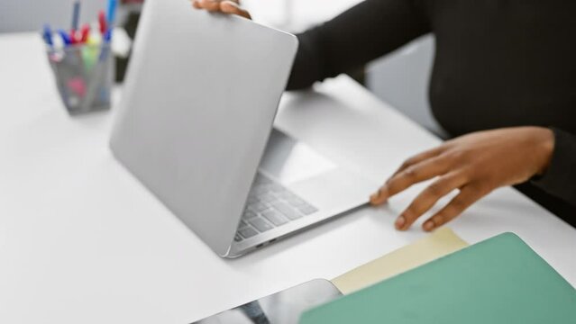 African american woman closing laptop in a modern office, indicating end of work day
