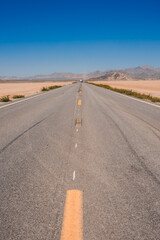 Scenic road through arid landscape with clear blue sky, tire marks on asphalt, leading towards...