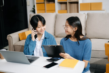 Fashion blogger concept, Two Asian women selling clothes on video streaming.Startup small business SME, using smartphone or tablet taking receive and checking.