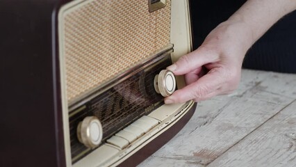 A close-up view of a woman's hand tuning the knobs on an old-fashioned radio set against a simple background, evoking a sense of nostalgia.