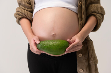 Portrait of Beautiful pregnant woman holding avocado over white background studio, health and maternity concept.