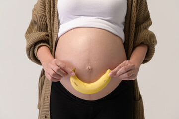Portrait of Beautiful pregnant woman holding banana over white background studio, health and maternity concept.