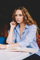 Serious female student sitting with modern laptop device in coworking space and pondering on information from website, concentrated hipster girl with curly hair waiting antivirus updating on netbook