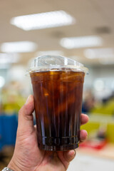 Holding disposable iced black coffee in plastic cup before drinking.
