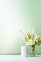 A minimalist still life image of a clear glass vase of white flowers on a white table against a pale green background.