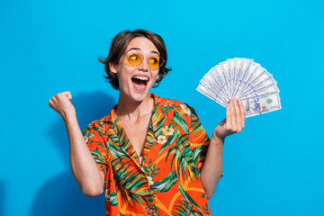Photo of overjoyed wealthy lady raise fist hold dollar bills look empty space ad isolated on blue...