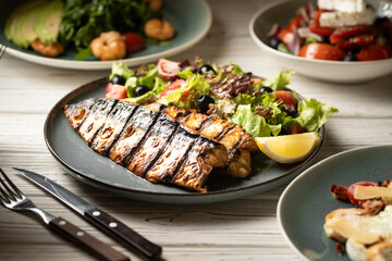 Grilled mackerel fillets with vegetables and lemon on blue plate in restaurant.