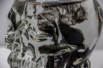 trickles, curls, figures and waves of black paint falling from above in a transparent glass jar in...