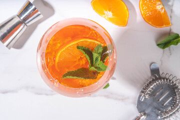 Classic italian aperitif aperol spritz cocktail in glass with ice cubes, alcohol sweet long alcohol drink with slice of orange and mint, on white background with hard light and bar utensils